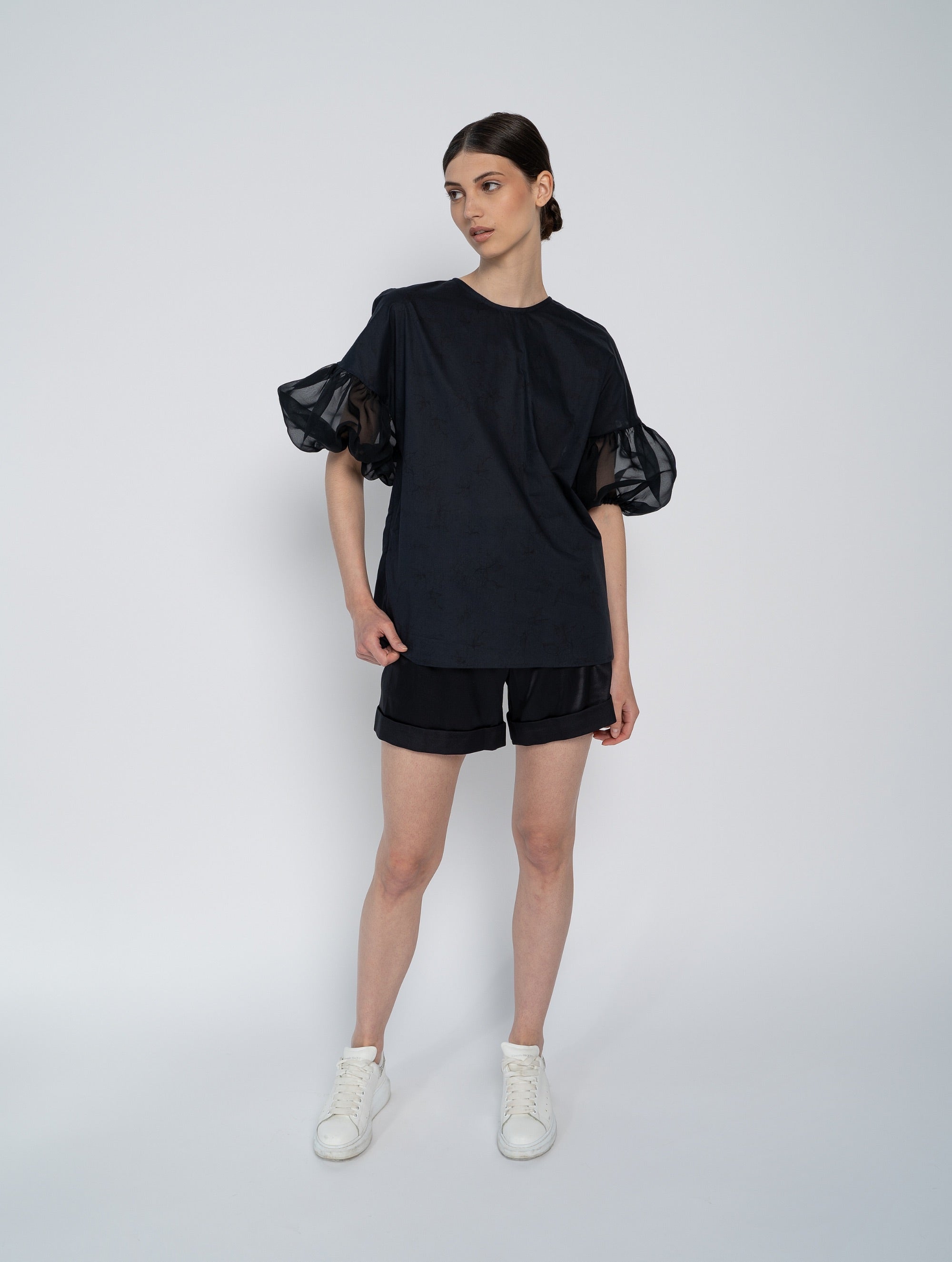 Schwarze Bluse mit Rundhalsausschnitt, Organza-Ärmeln, Seitenschlitzen und versteckten Seitentaschen.