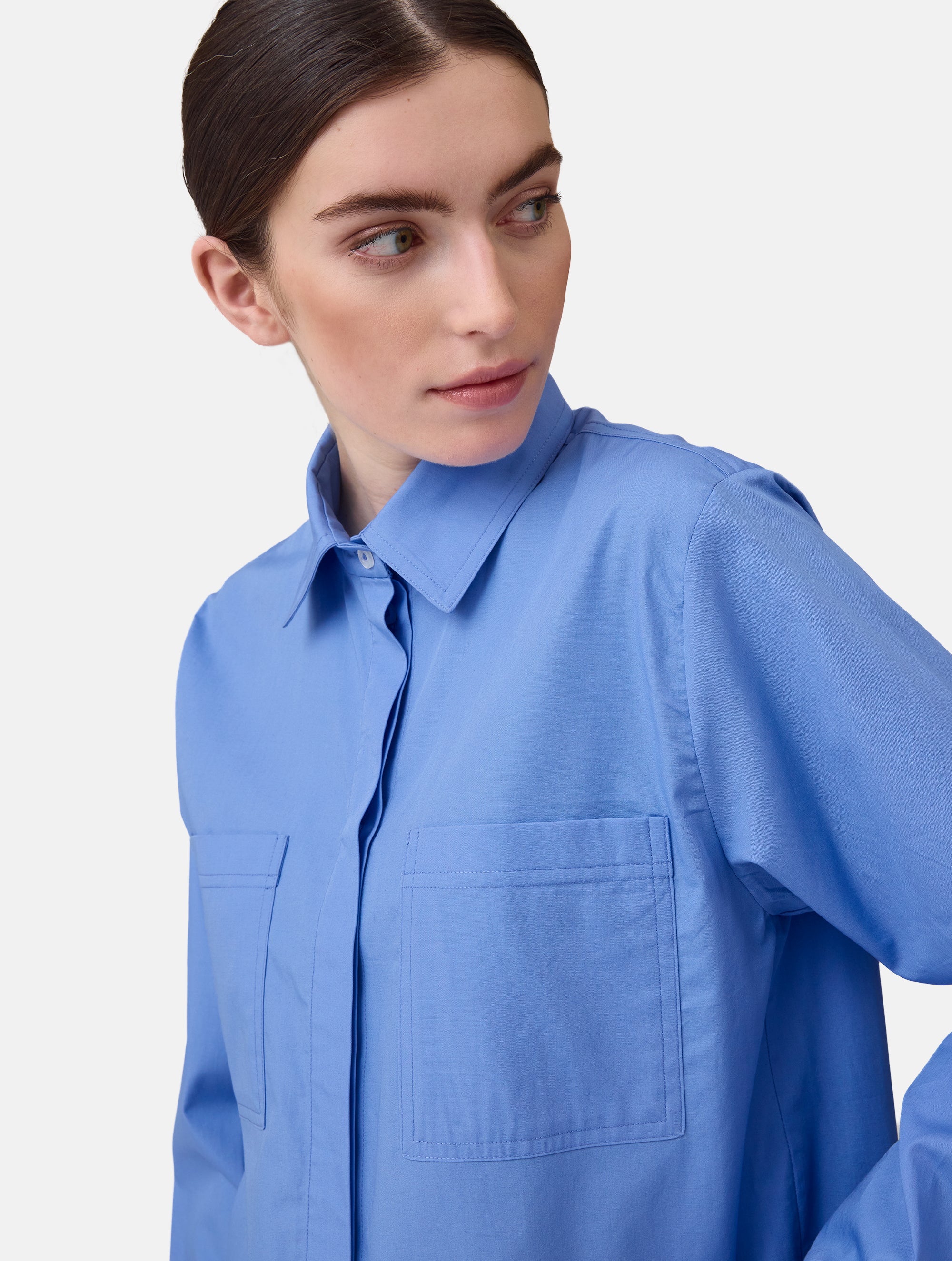 Langes Oversize Blusenhemd mit klassischem Hemdkragen und Manschetten, sowie zwei aufgesetzten Brutstaschen und abgerundeten Saumende im Rückteil. Dieses Modell ist Teil unserer REBORN-Linie und steht für unsere "Zero-Waste-Politik", da mit Stoff aus Altbestand gefertigt.