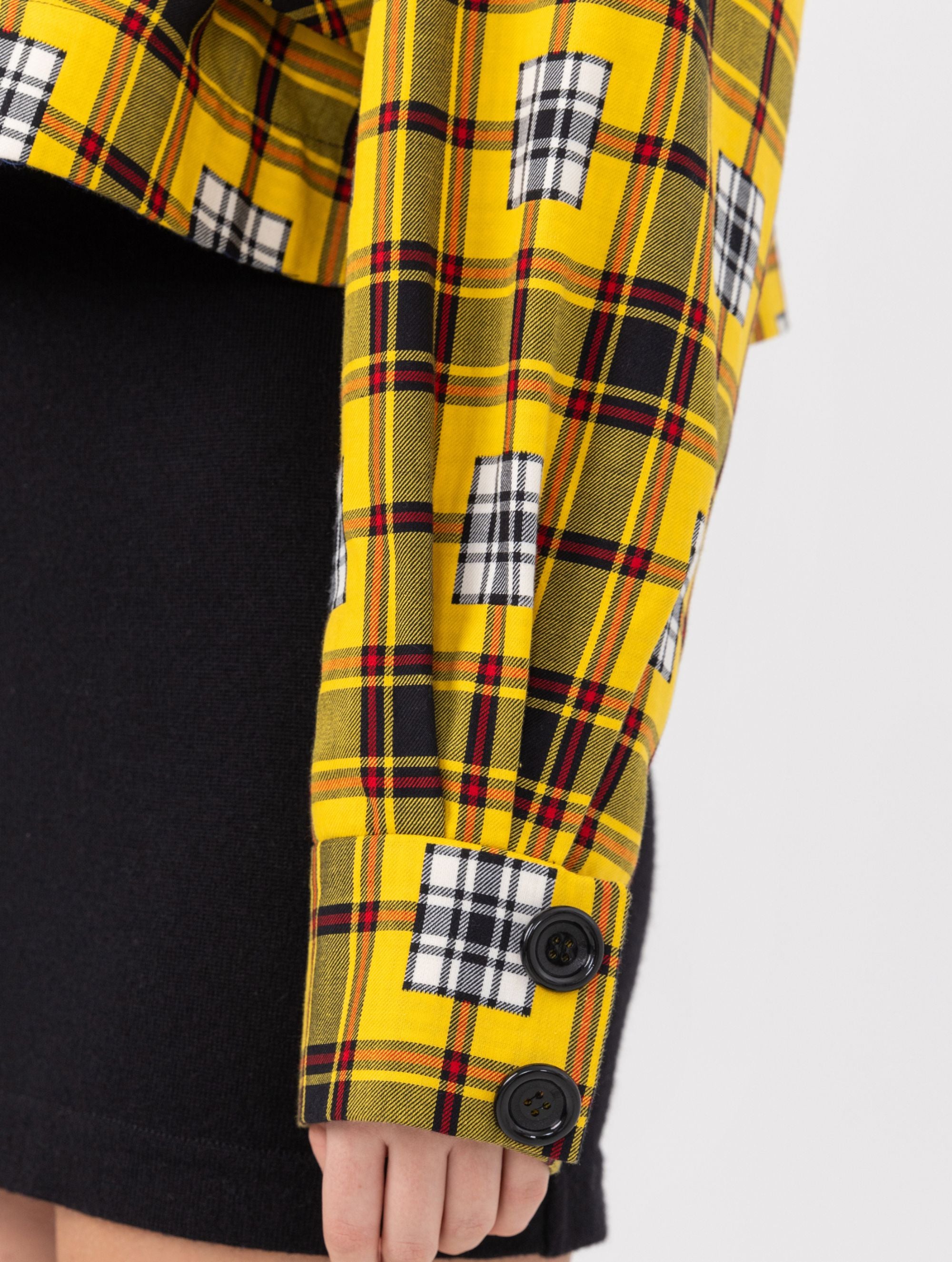 Doppelseitige Karo-Kurzjacke mit abnehmbaren Schulterpolstern, eingesetzten Ärmeln mit Ärmelgürteln und Schulterklappen sowie vorderen Halbpasse. Die Jacke kann von beiden Seiten getragen werden. Hergestellt aus Naturfasern.