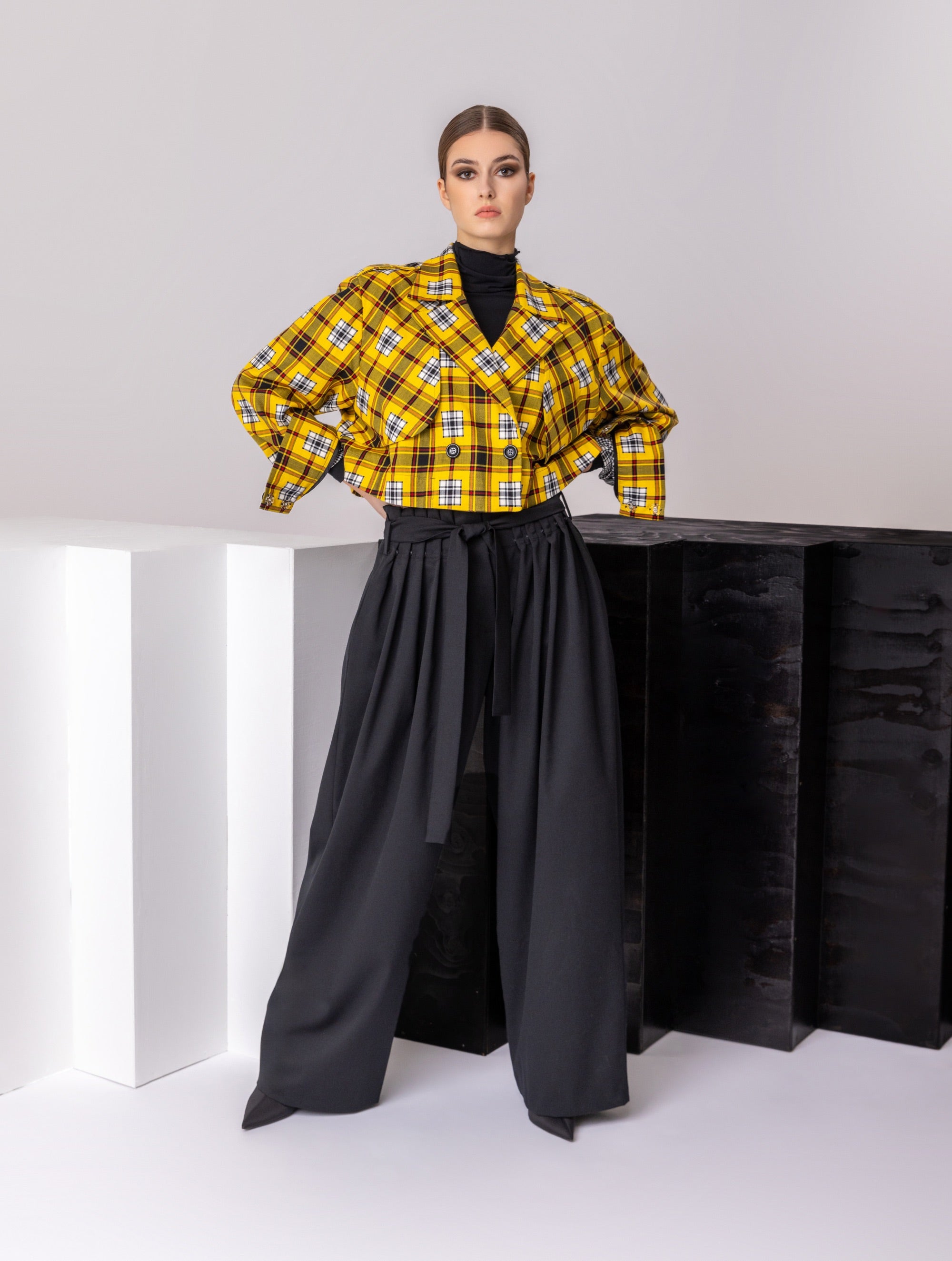 Doppelseitige Karo-Kurzjacke mit abnehmbaren Schulterpolstern, eingesetzten Ärmeln mit Ärmelgürteln und Schulterklappen sowie vorderen Halbpasse. Die Jacke kann von beiden Seiten getragen werden. Hergestellt aus Naturfasern.