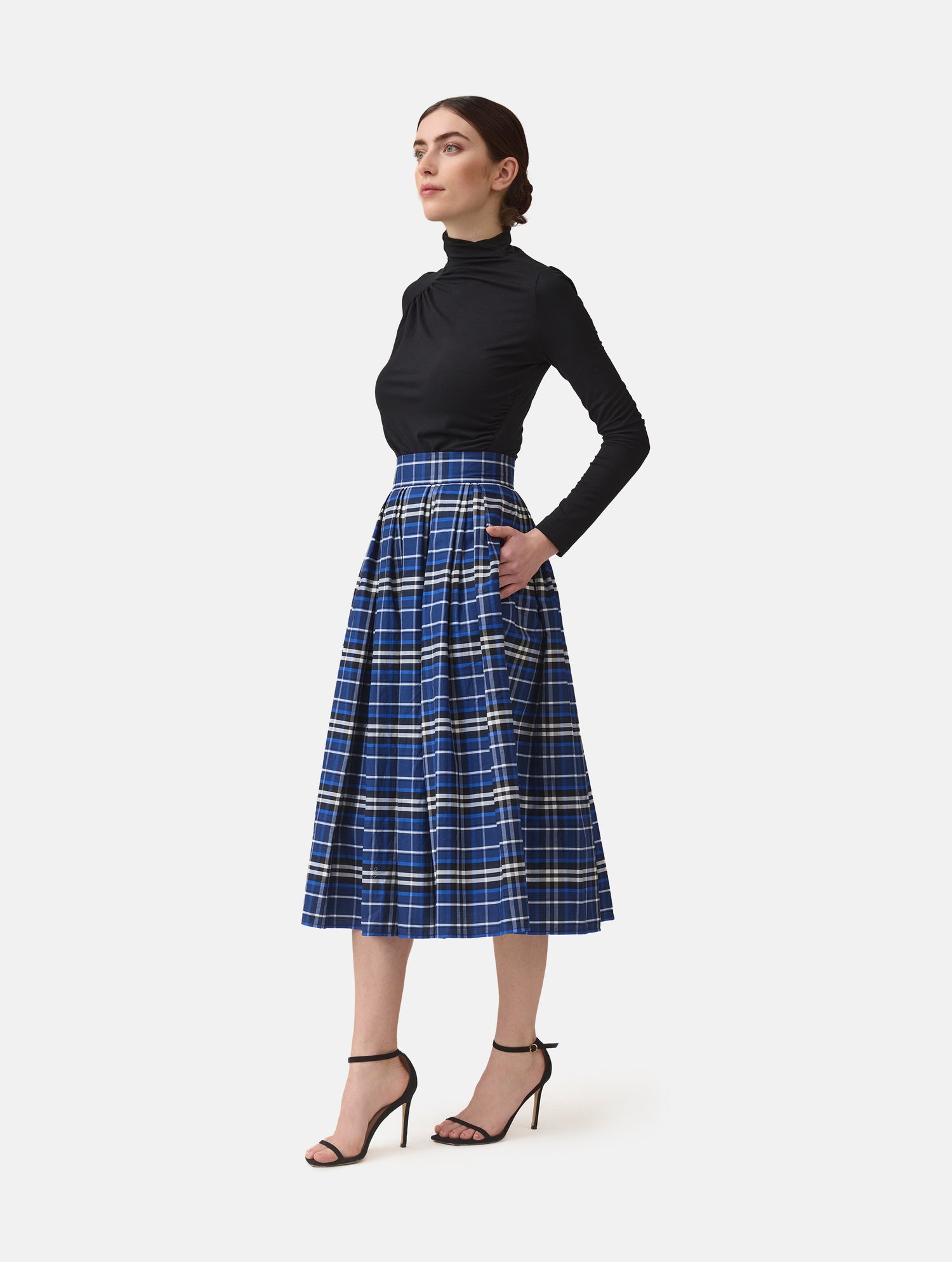 Weit ausgestellter Midirock aus karierter Baumwolle mit in Falten gelegtem und tailliertem Rockbund, versteckten Taschen in der Seitennaht, sowie einem Reißverschluß auf der Rückseite. Dieses Modell ist Teil unserer REBORN-Linie und steht für unsere "Zero-Waste-Politik", da mit Stoff aus einem Deadstock stammt.