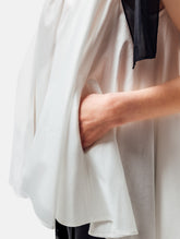 Weit geschnittenes Tanktop aus weißer Baumwolle mit schwarzem Schleifendetail und seperaten Gürtel aus schwarzer Baumwolle. Versteckte Seitentaschen in den Seitennähten. Dieses Produkt ist Teil unserer Reborn Linie.