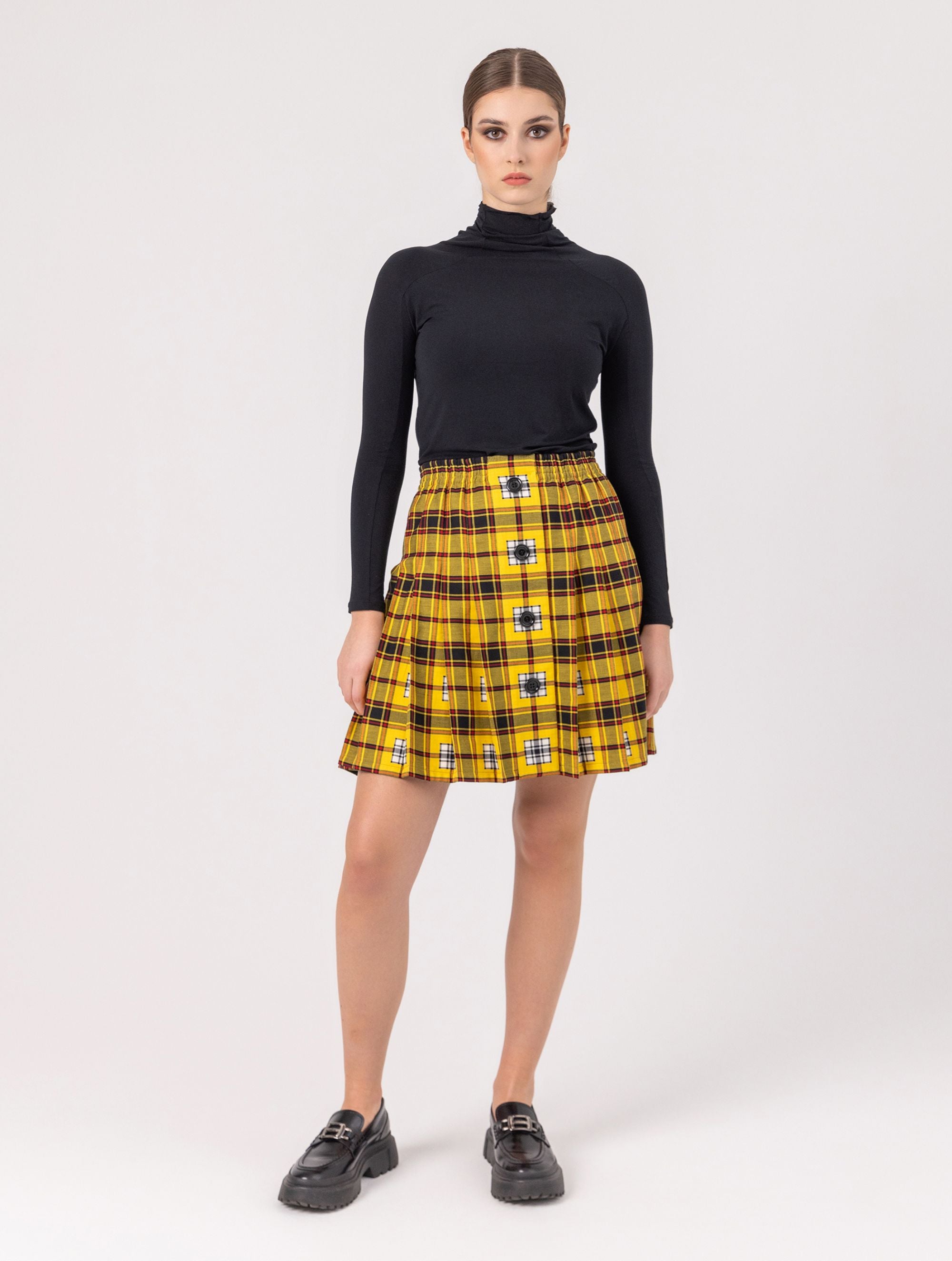 Doppelseitig karierter Faltenminirock mit elastischem Bund und Knopfleiste auf der Vorderseite. Der Rock kann von beiden Seiten getragen werden. Hergestellt aus Naturfasern.
