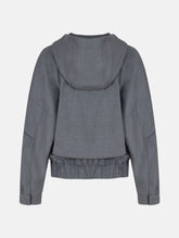 Locker geschnittene Blousonjacke mit Kapuze und Reißverschluss, sowie dreiecksförmiger Kängurutasche im Vorderteil und elastischem Bündchen am Saumende. Dieses Modell ist Teil unserer REBORN-Linie und steht für unsere "Zero-Waste-Politik", da mit Stoff aus Altbestand gefertigt.