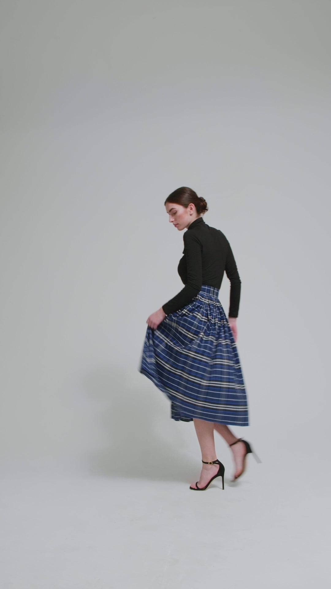 Weit ausgestellter Midirock aus karierter Baumwolle mit in Falten gelegtem und tailliertem Rockbund, versteckten Taschen in der Seitennaht, sowie einem Reißverschluß auf der Rückseite. Dieses Modell ist Teil unserer REBORN-Linie und steht für unsere "Zero-Waste-Politik", da mit Stoff aus einem Deadstock stammt.