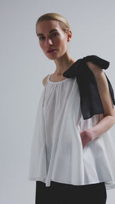 Weit geschnittenes Tanktop aus weißer Baumwolle mit schwarzem Schleifendetail und seperaten Gürtel aus schwarzer Baumwolle. Versteckte Seitentaschen in den Seitennähten. Dieses Produkt ist Teil unserer Reborn Linie.