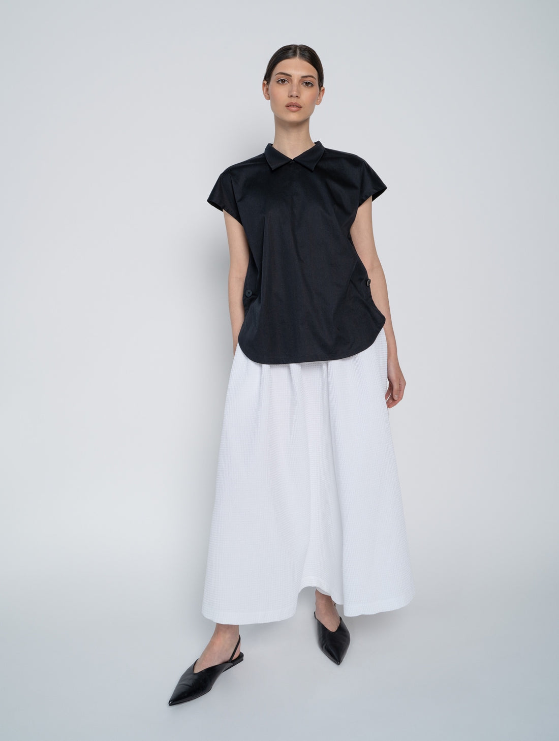 Schwarze, ärmellose Bluse mit Flügelkragen und Knöpfen auf der Vorderseite neben der Seitennaht.
