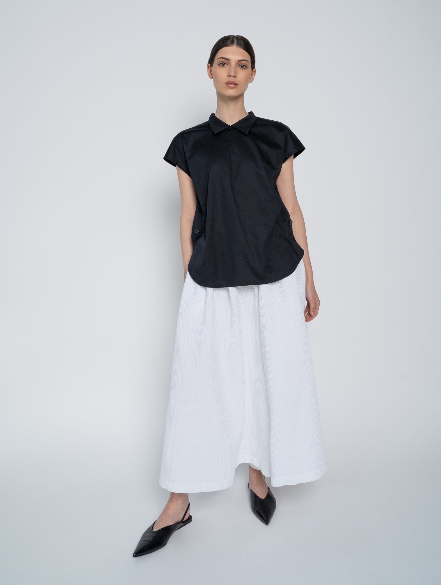 Schwarze, ärmellose Bluse mit Flügelkragen und Knöpfen auf der Vorderseite neben der Seitennaht.