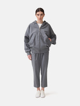 Locker geschnittene Blousonjacke mit Kapuze und Reißverschluss, sowie dreiecksförmiger Kängurutasche im Vorderteil und elastischem Bündchen am Saumende. Dieses Modell ist Teil unserer REBORN-Linie und steht für unsere "Zero-Waste-Politik", da mit Stoff aus Altbestand gefertigt.