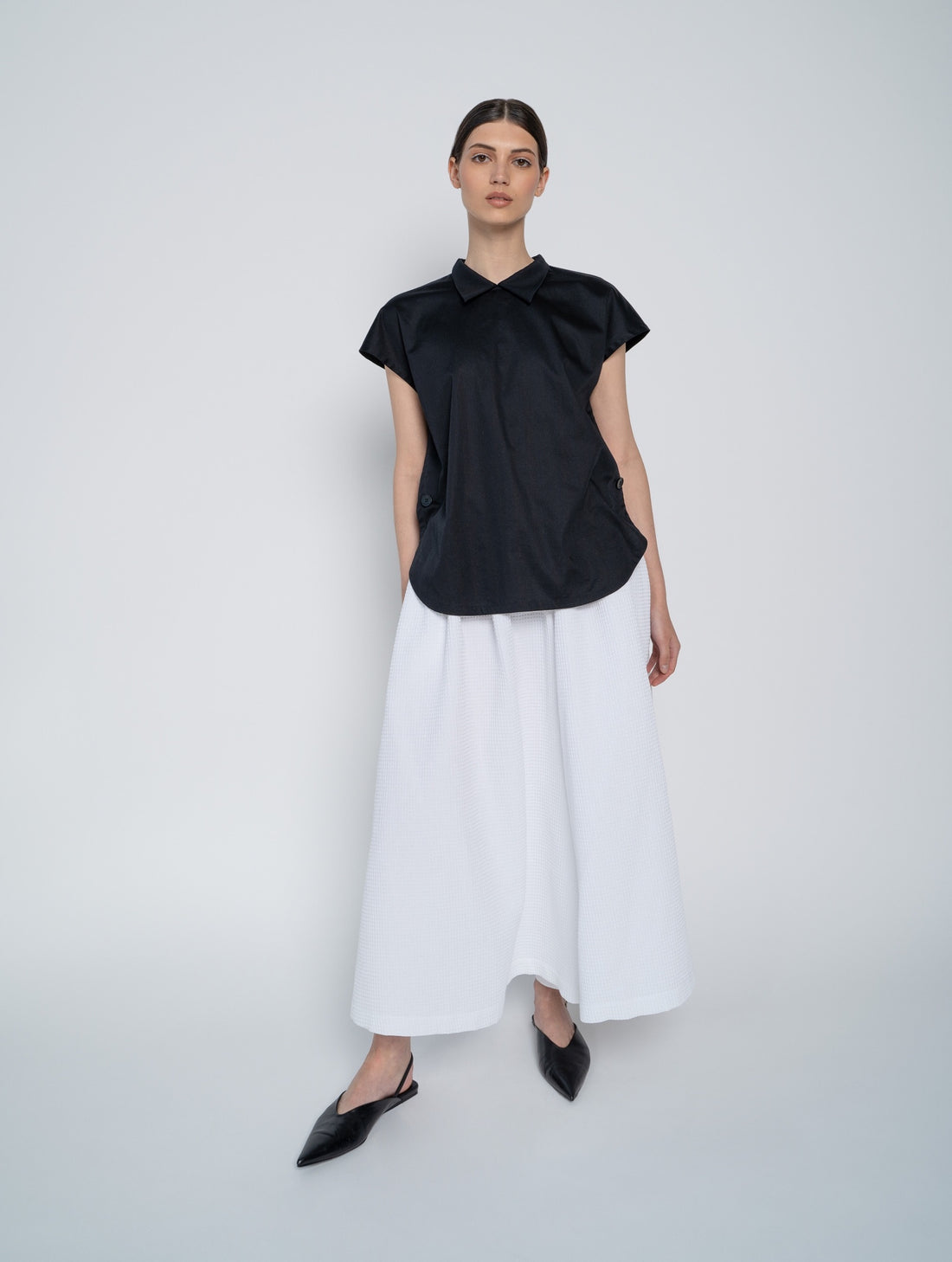 Schwarze, ärmellose Bluse mit Flügelkragen und Knöpfen auf der Vorderseite neben der Seitennaht.