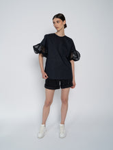 Schwarze Bluse mit Rundhalsausschnitt, Organza-Ärmeln, Seitenschlitzen und versteckten Seitentaschen.