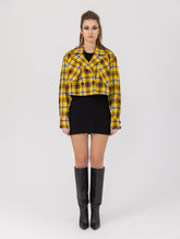 Doppelseitige Karo-Kurzjacke mit abnehmbaren Schulterpolstern, eingesetzten Ärmeln mit Ärmelgürteln und Schulterklappen sowie vorderen Halbpasse. Die Jacke kann von beiden Seiten getragen werden.   Hergestellt aus Naturfasern. 