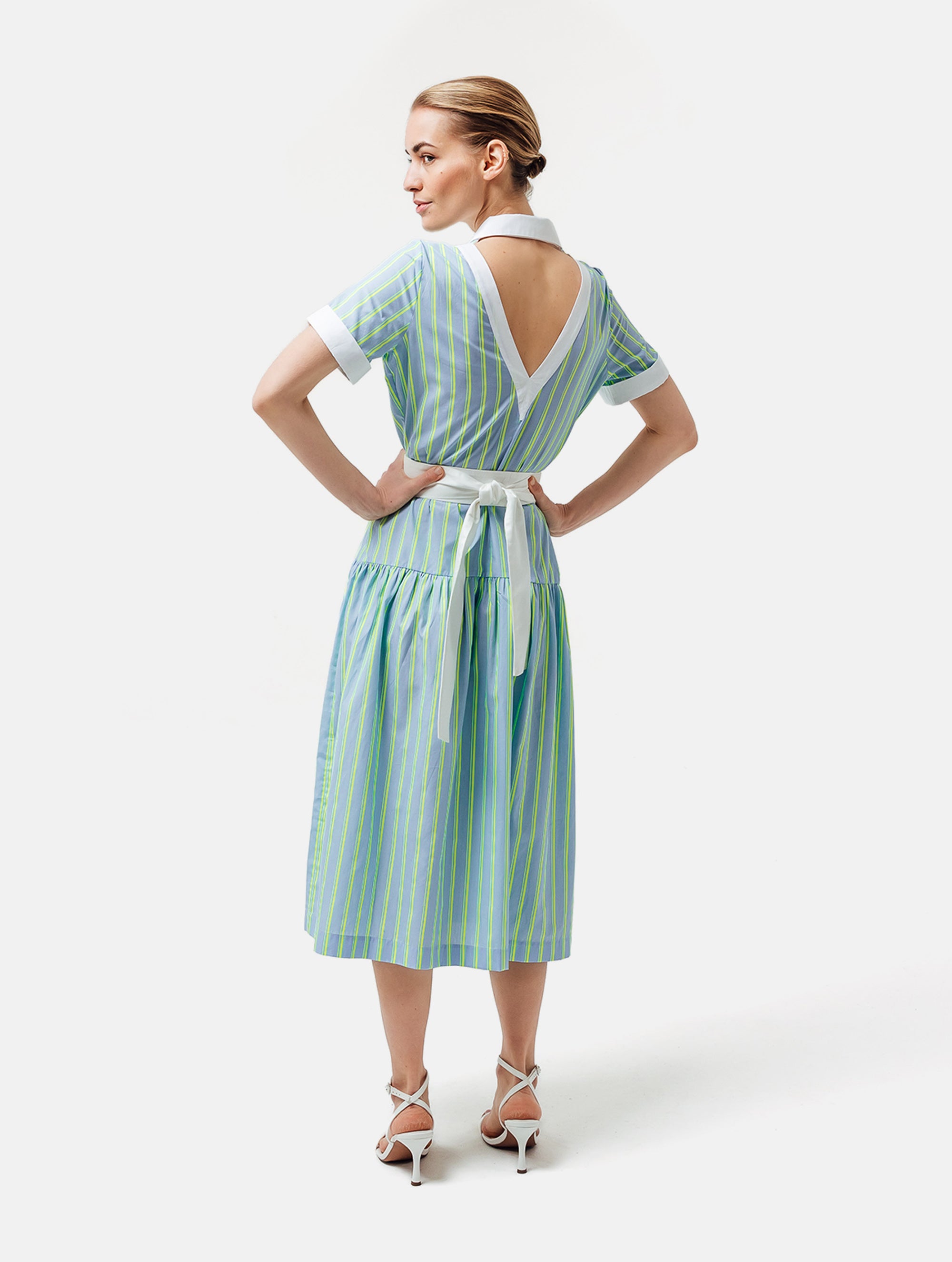 Gestreiftes Midikleid mit weiß abgesetzten Reverskragen, sowie Ärmelenden, raffiniertem Rückenausschnitt, verdeckter Knopfleiste, tragbar mit und ohne Gürtel aus weißer Baumwolle. Stoffe kommen aus dem Altbestand der Firma, daher nachhaltig.