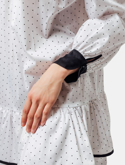 Grade geschnittenes Minikleid aus gepunkteter Baumwolle mit farblich abgesetzten Kragen und Manschetten aus schwarzer Chiffonseide, sowie doppelten Volantssaum. 