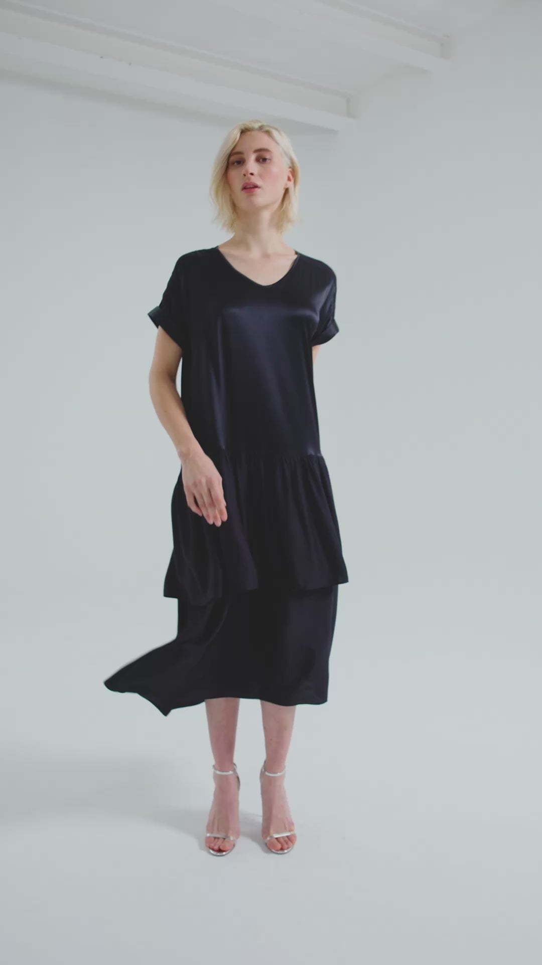 Locker fallendes Kurzarmkleid mit V-Ausschnitt und Volantrock aus Seidensatin und Viskose. Dieses Produkt ist Teil unserer Reborn Linie.